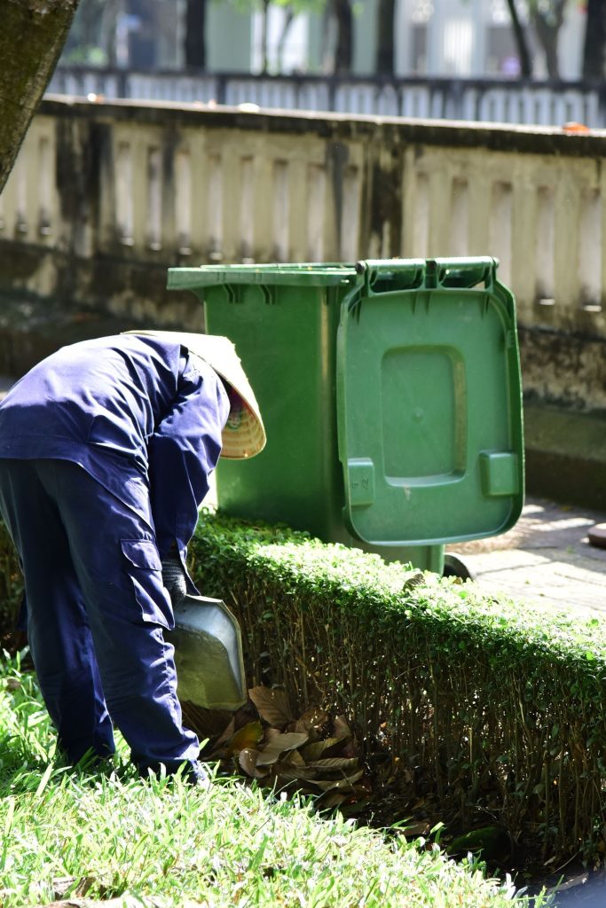 Gardener collecting clippings next to a green waste bin