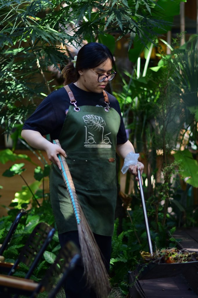 Gardener in an apron watering plants with a garden hose