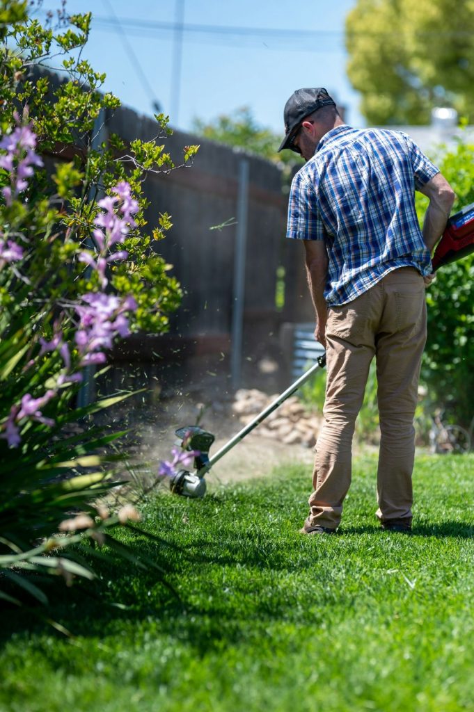 Gardener edging a lawn with a string trimmer near flower beds